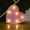 A pink heart-shaped LED night light with glowing white lights on a wooden surface.
