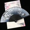 A vintage silk folding fan with gray and black oriental patterns is displayed against a light background.