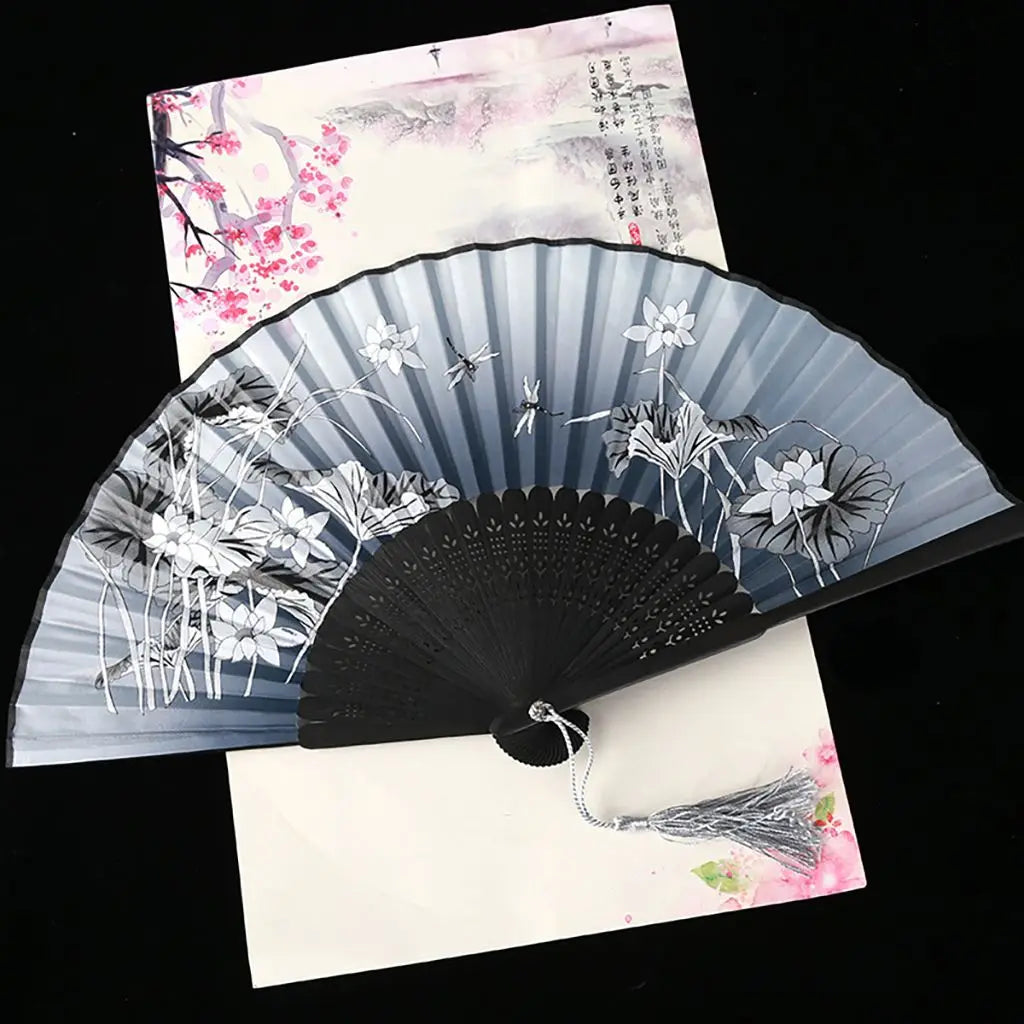 A vintage silk folding fan with gray and black oriental patterns is displayed against a light background.
