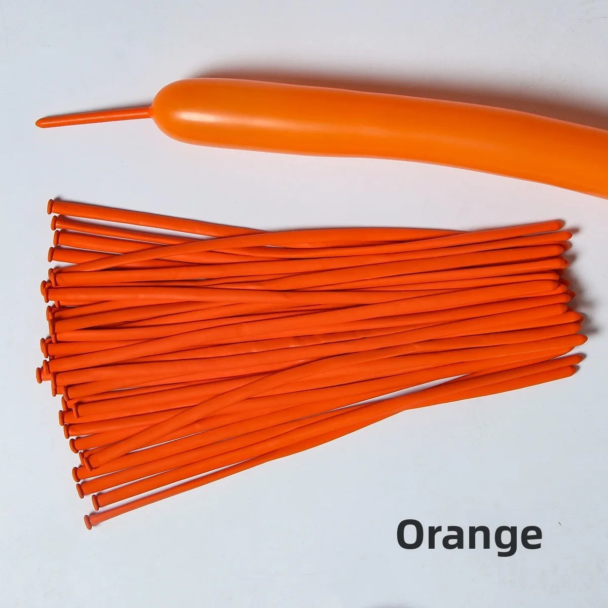 A collection of orange latex strip balloons and one long orange balloon are displayed on a white surface.