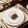A set of silver embossed charger plates is displayed on a table with a plated steak and silverware.