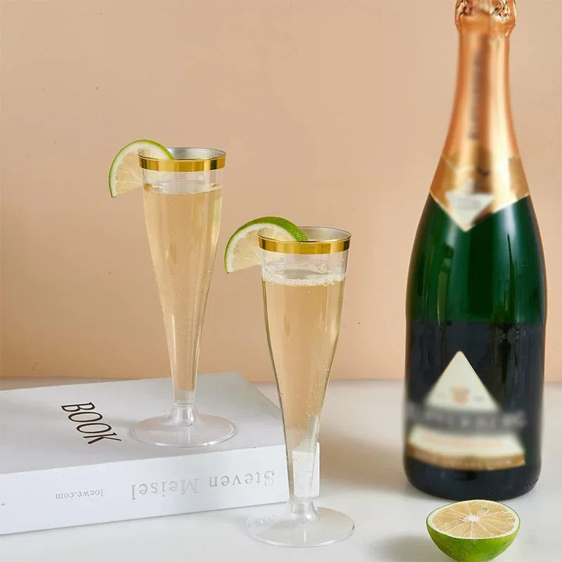 A set of two clear plastic champagne flutes and a bottle of sparkling wine on a white surface.