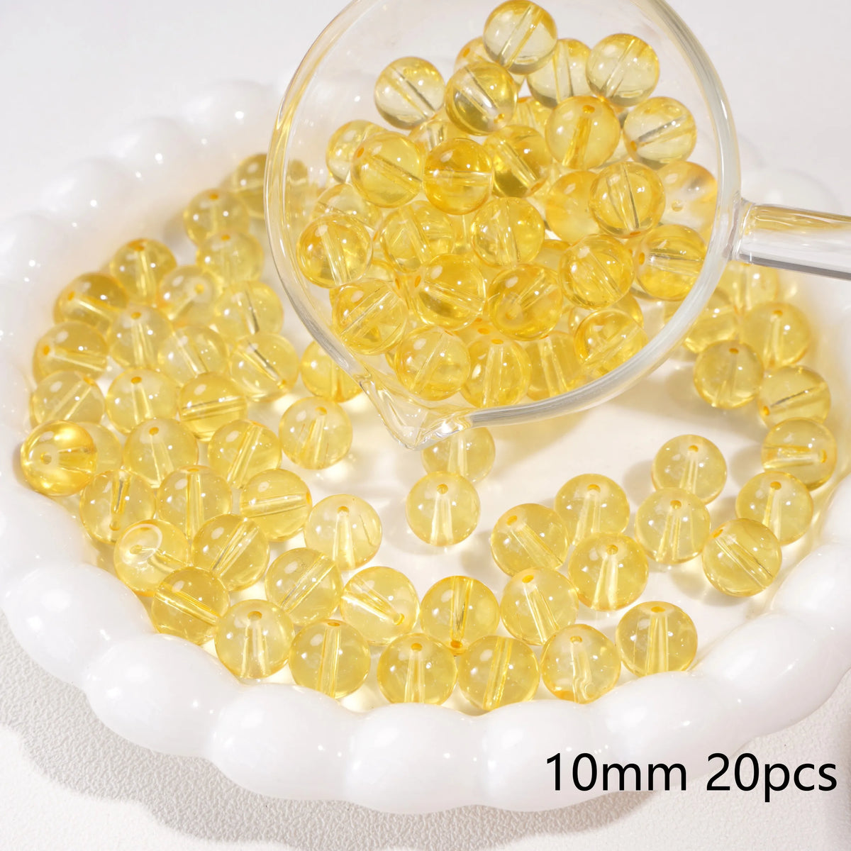 A clear glass dropper holds numerous round yellow spacer beads scattered on a white surface.