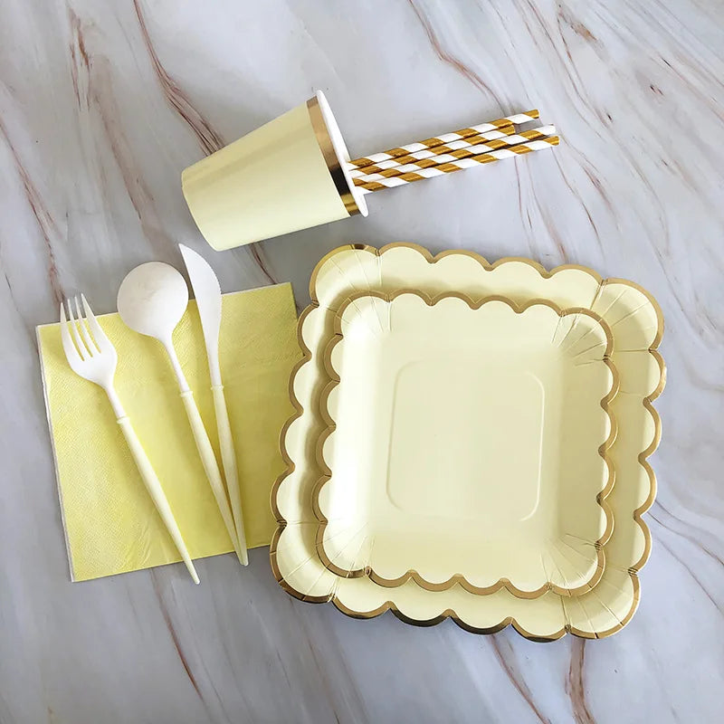 A gold disposable party tableware set including plates, napkins, cups, and straws arranged on a marble surface.