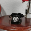 A black retro rotary desk phone miniature is placed on a wooden surface.