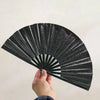 A hand is opening a black glitter holographic fan, showing radiating lines of light.