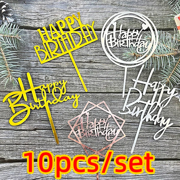 Un juego de diez toppers para pastel de cumpleaños acrílicos en rosa y dorado, exhibidos sobre un fondo de madera.