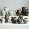A collection of vintage dual-sided ceramic vases in various earthy tones and textures displayed on a white surface.