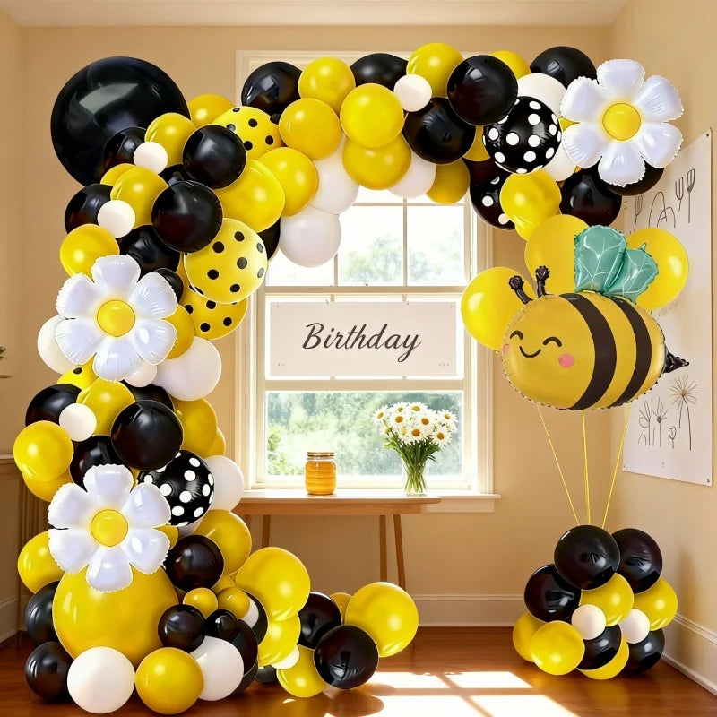 A yellow and black balloon arch set featuring bees and daisies arranged around a window.