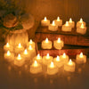 A collection of glowing white LED tea light candles arranged on a wooden surface with a floral arrangement in the background.