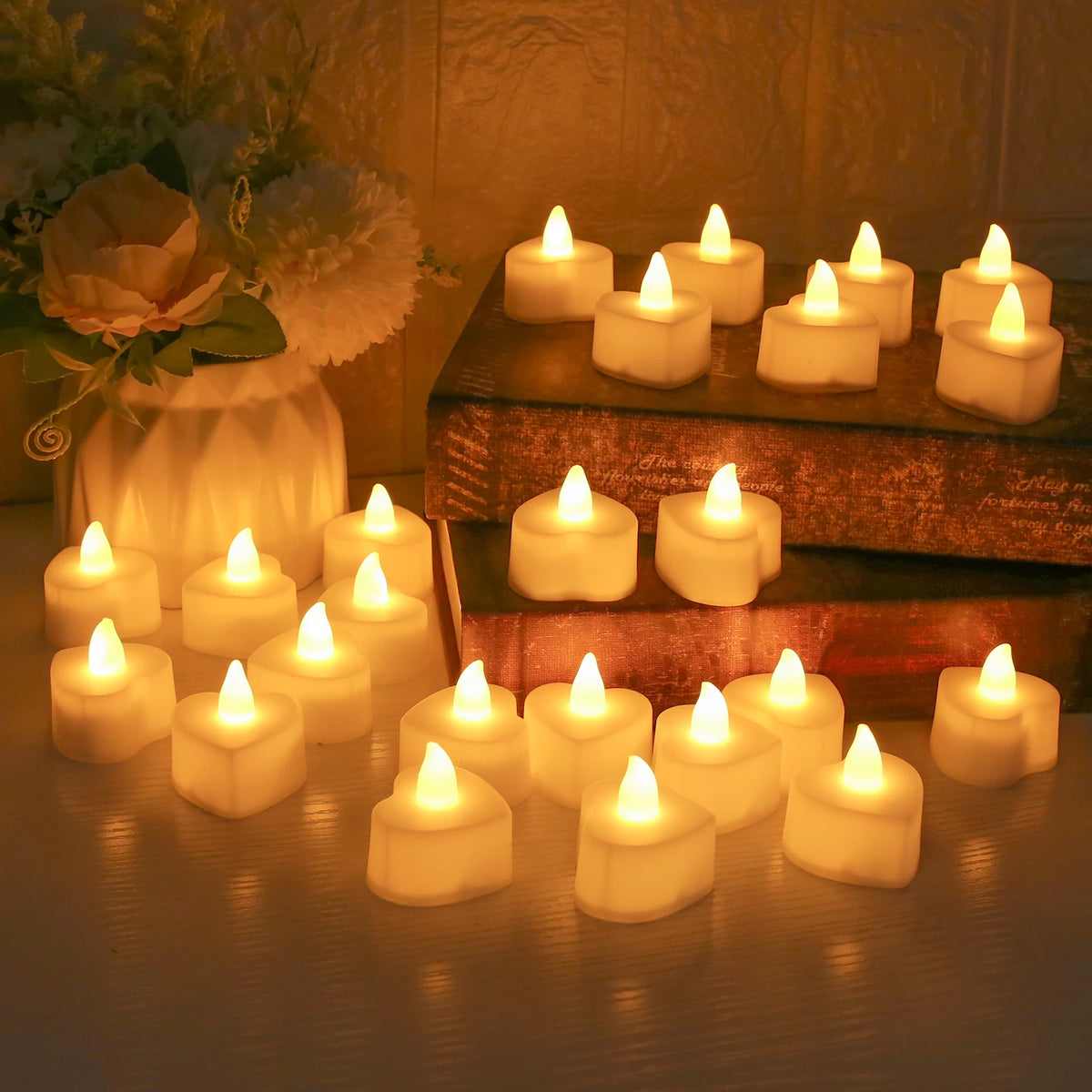 A collection of glowing white LED tea light candles arranged on a wooden surface with a floral arrangement in the background.