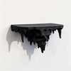 A black, dripping skull wall shelf with a gothic floating display design casting a shadow on a white wall.