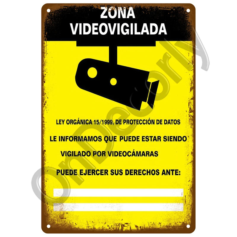 A yellow metal sign with black text warning that the area is video-surveilled by cameras under organic law.