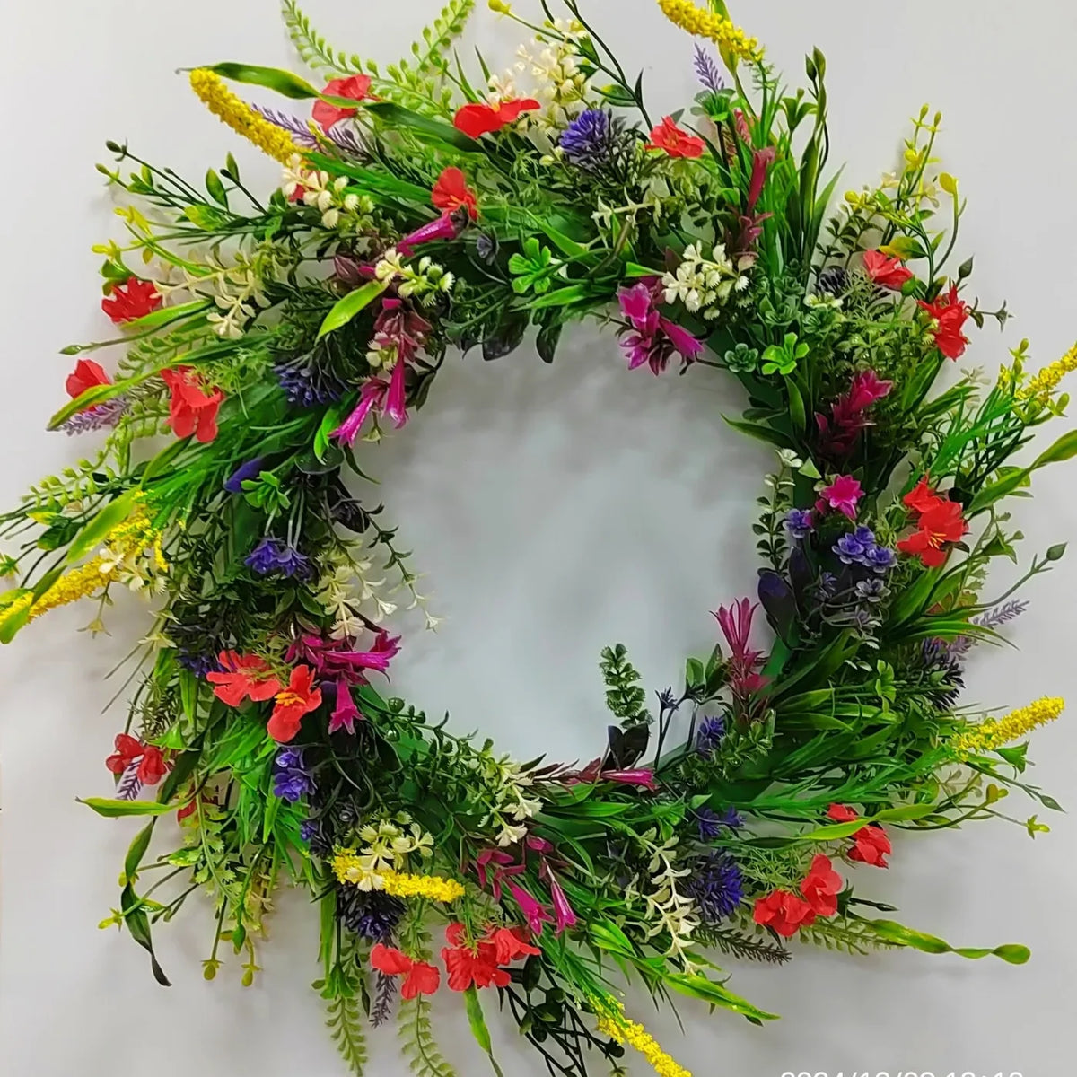 A wreath of artificial wildflowers featuring red, purple, yellow, and green foliage for spring and summer decor.