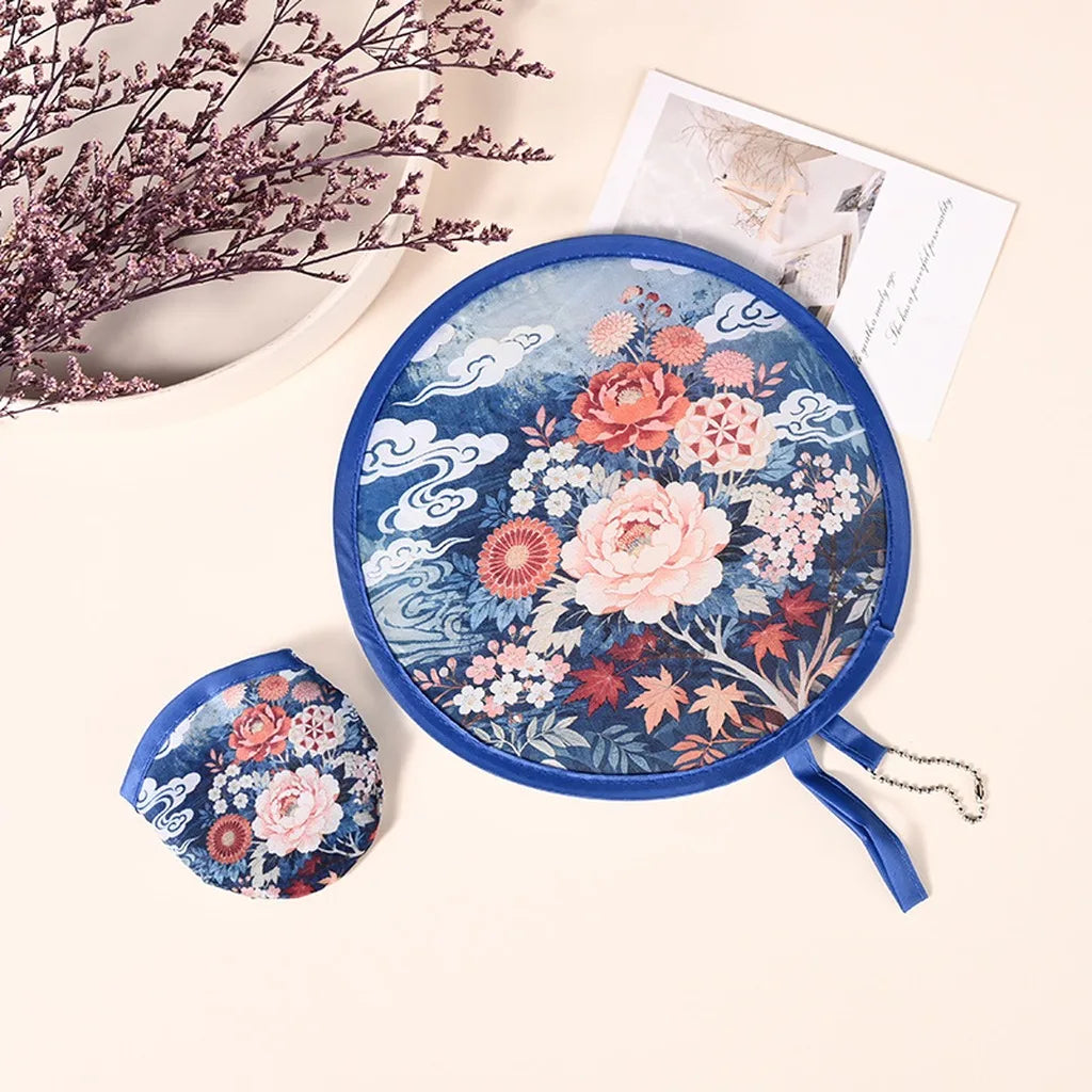 A blue fabric cooling fan with a floral and cloud pattern is shown next to a white card and dried branches.