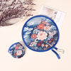 A blue fabric cooling fan with a floral and cloud pattern is shown next to a white card and dried flowers.