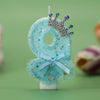 A light blue glitter candle decoration shaped like the number 8 with a silver crown and sheer blue netting.