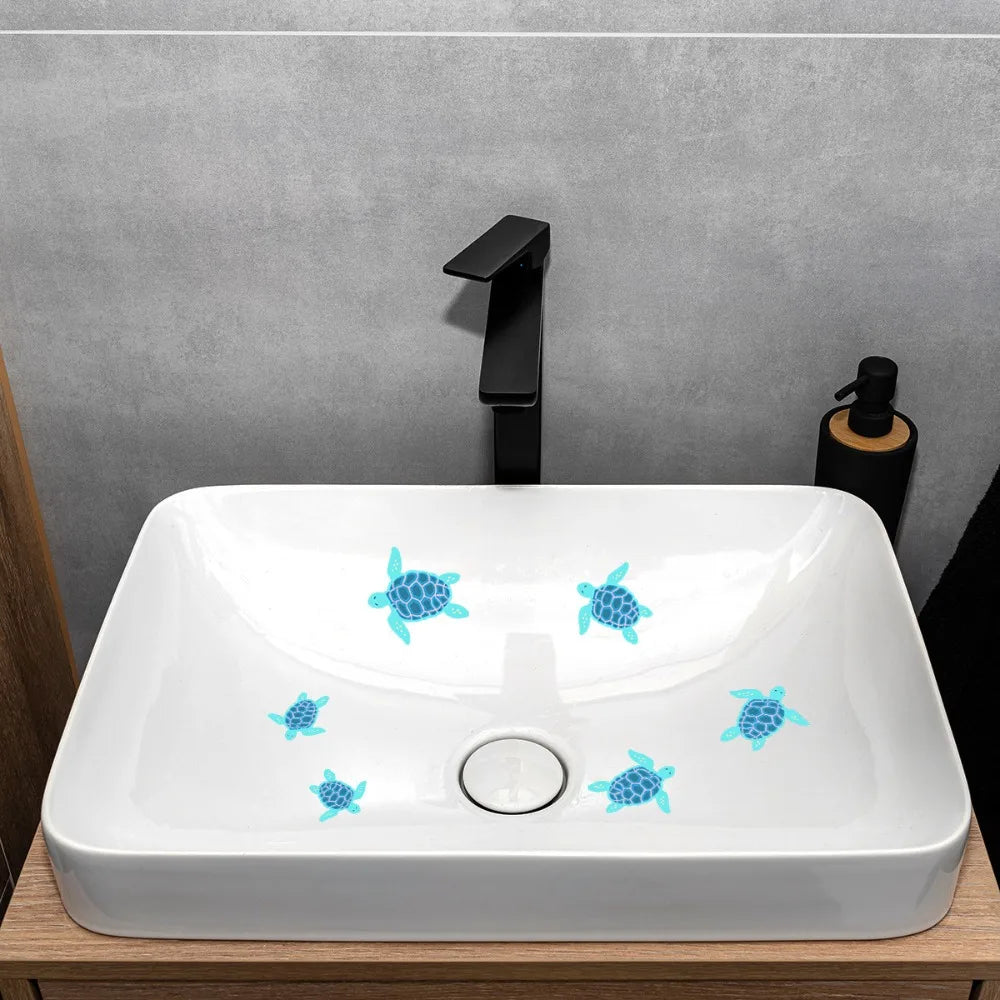 A white ceramic bathroom sink with blue glow-in-the-dark sea turtle decals and a black faucet mounted on a gray wall.
