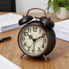A vintage twin-bell alarm clock with a dark wooden frame and distressed face sits on a wooden table.