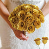 A bouquet of twelve golden glitter artificial roses held by a person in a white dress.