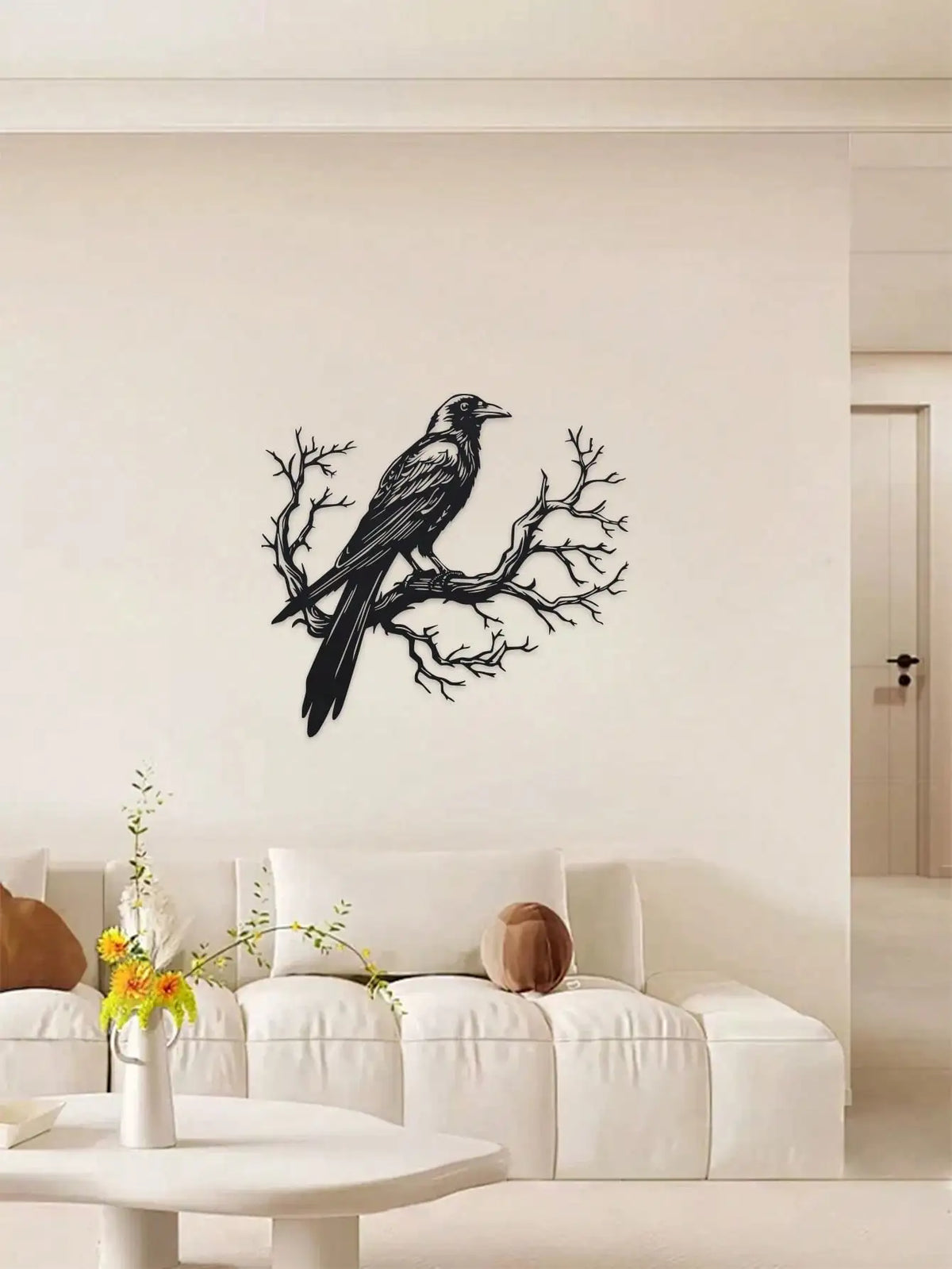 Black raven perched on a bare tree branch metal wall art displayed above a white sofa.