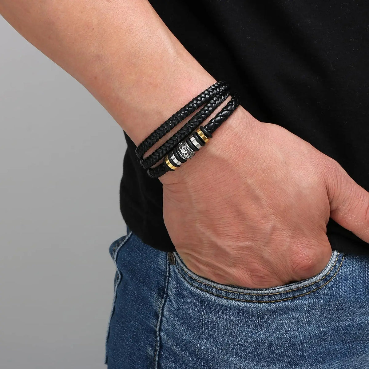 A close-up of a hand wearing a black braided leather cuff bracelet on the wrist.