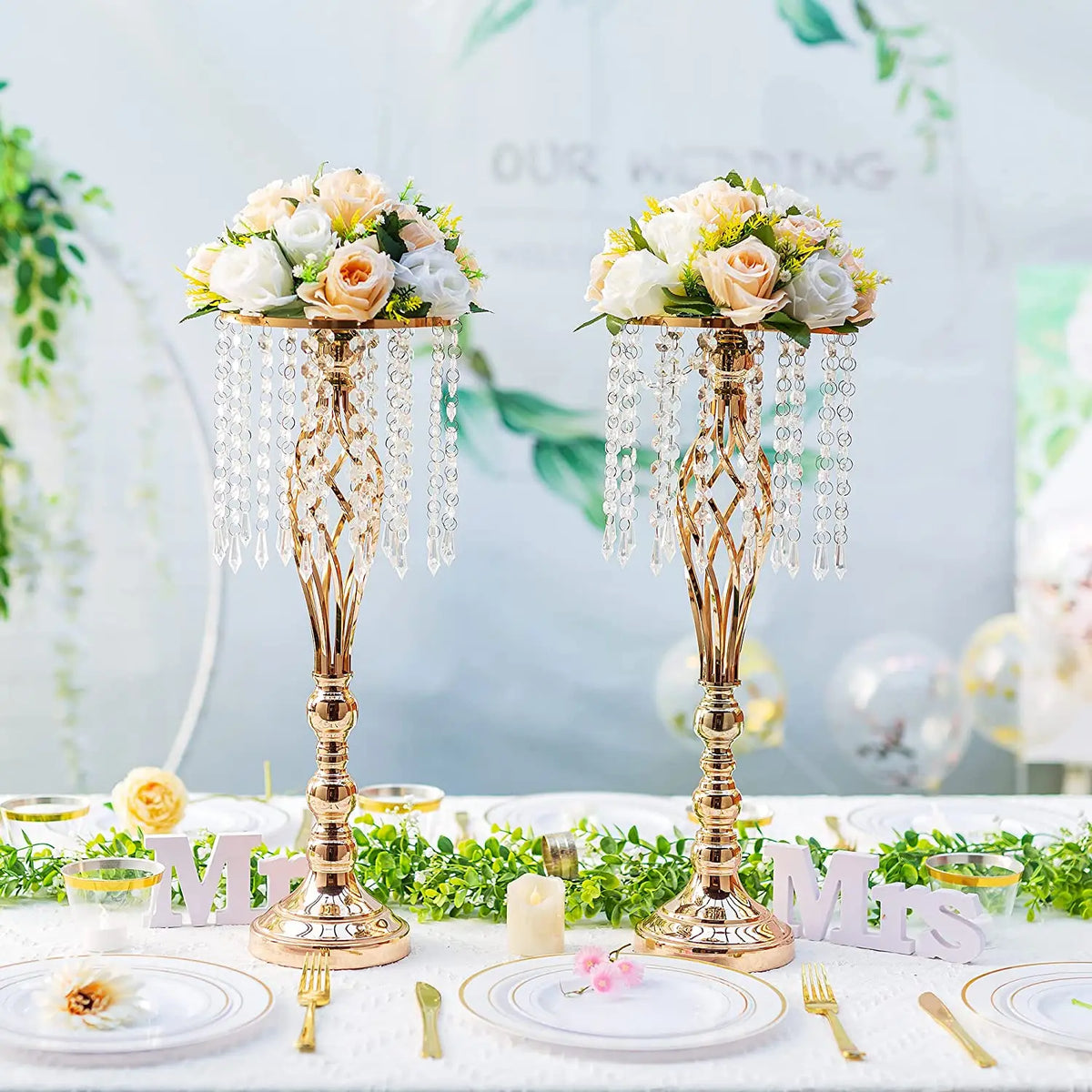 A set of gold crystal vases used as wedding centerpieces with floral arrangements on a white table.