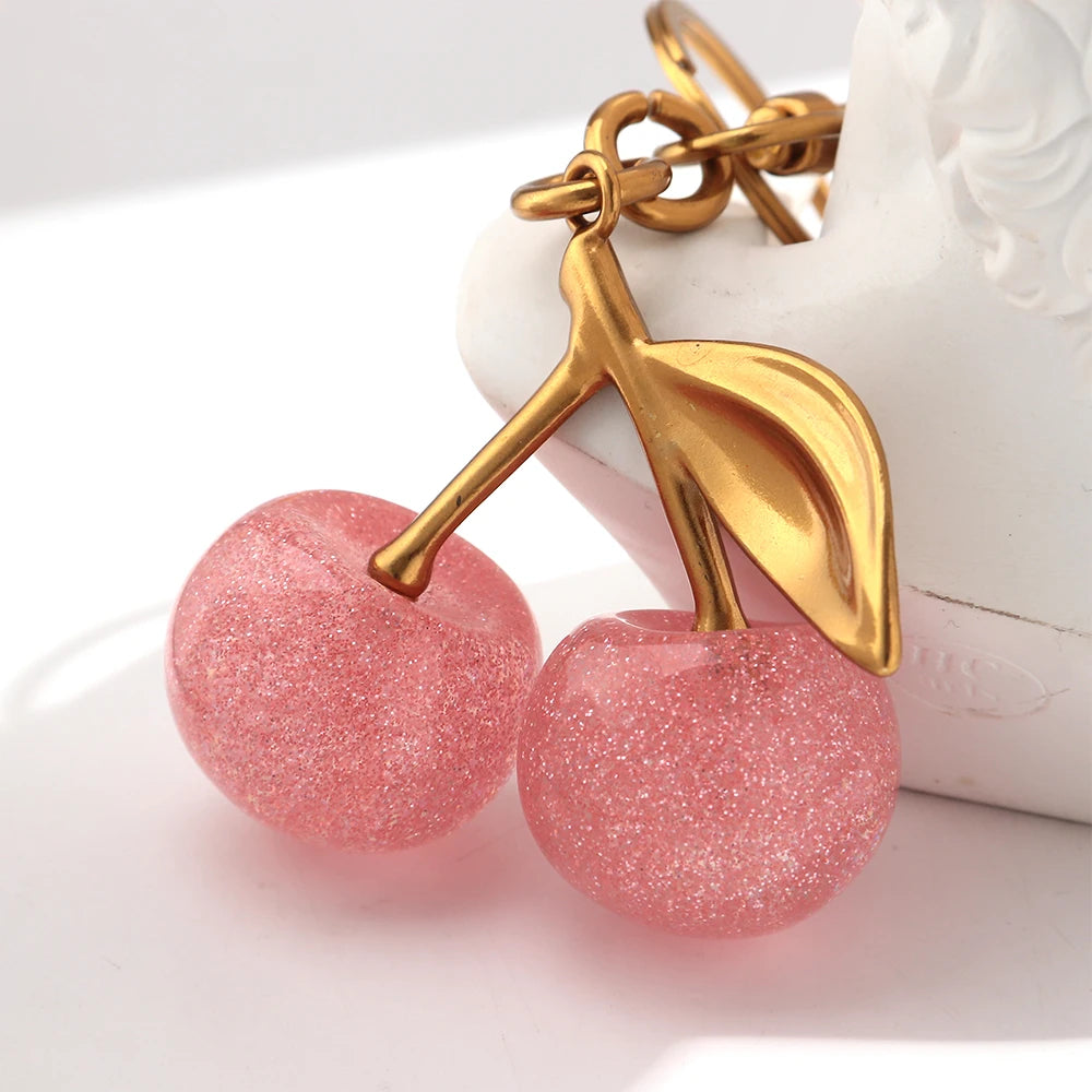 A pink cherry resin pendant keychain with a gold-colored leaf charm