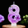 A purple glitter number eight candle decorated with a purple flower, set on a wooden surface.