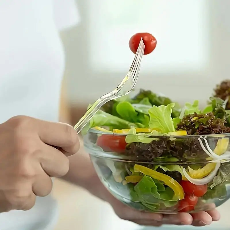 A hand holds a clear plastic dessert fork poised above a fresh salad with tomatoes and greens.