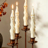 A set of three white soy candles shaped like ghosts and mummies displayed on brass candlesticks.