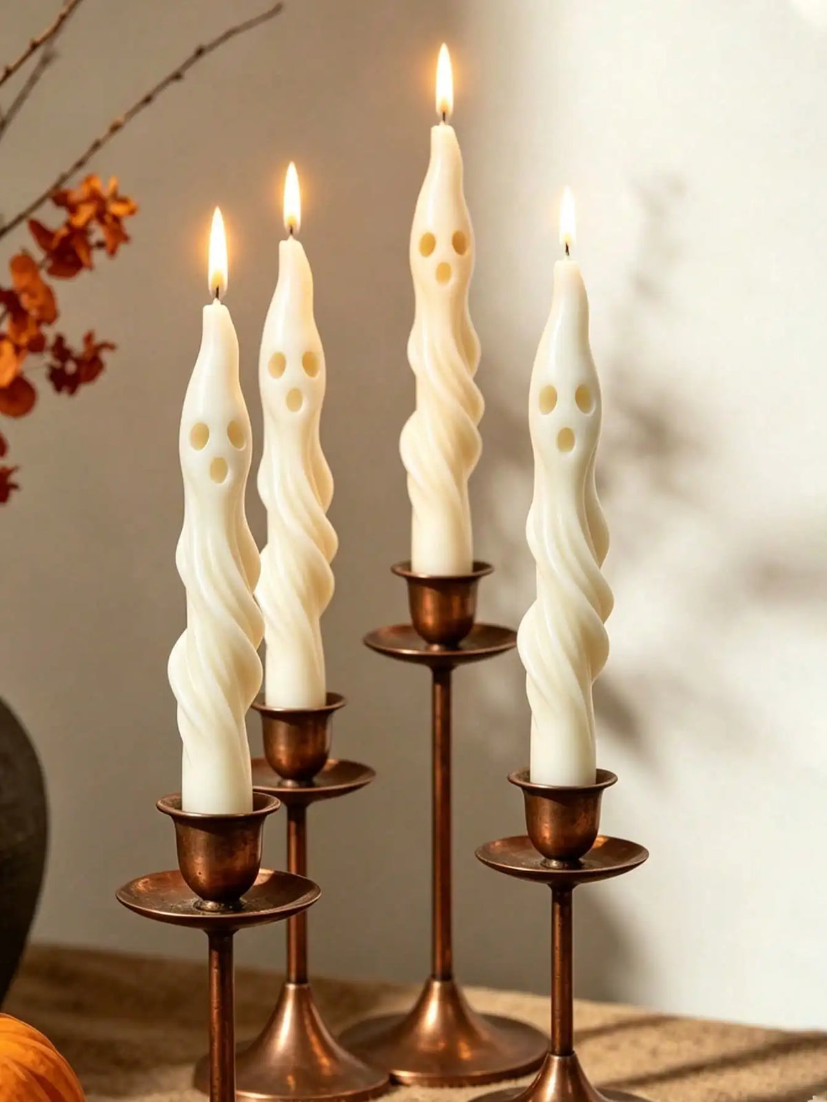 A set of three white soy candles shaped like ghosts and mummies displayed on brass candlesticks.