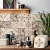 A kitchen backsplash featuring beige and brown patterned tile wall stickers with a dark mug and greenery.
