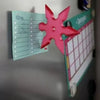 A pink 3D axe-shaped fridge magnet is displayed next to a green calendar board.