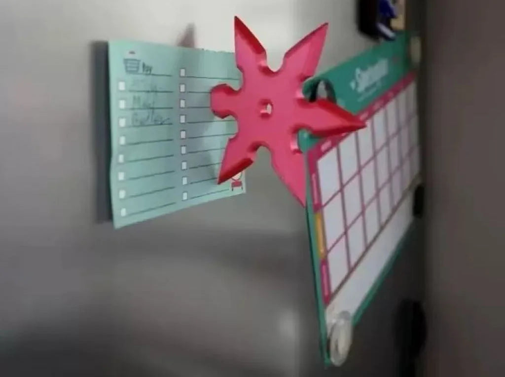 A pink 3D axe-shaped fridge magnet is displayed next to a green calendar board.