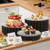 A black folding dessert table display stand holding various cupcakes and cakes on a wooden countertop.