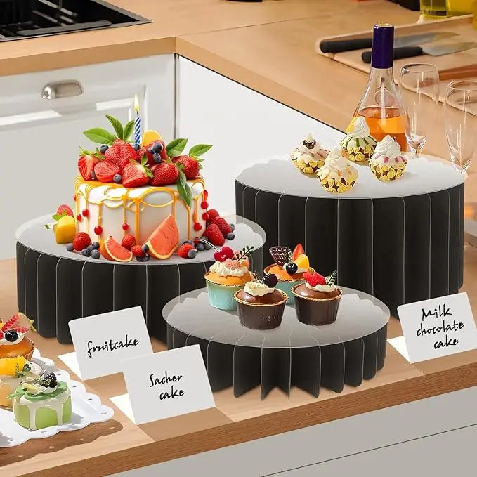 A black folding dessert table display stand holding various cupcakes and cakes on a wooden countertop.