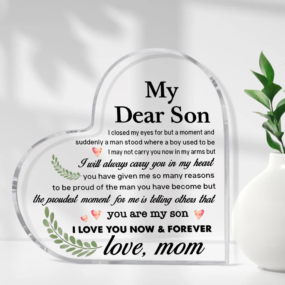 A clear heart-shaped acrylic keepsake plaque with engraved text expressing love and pride for a son.