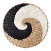 A round woven straw wall decor hanging featuring a black and white spiral design.