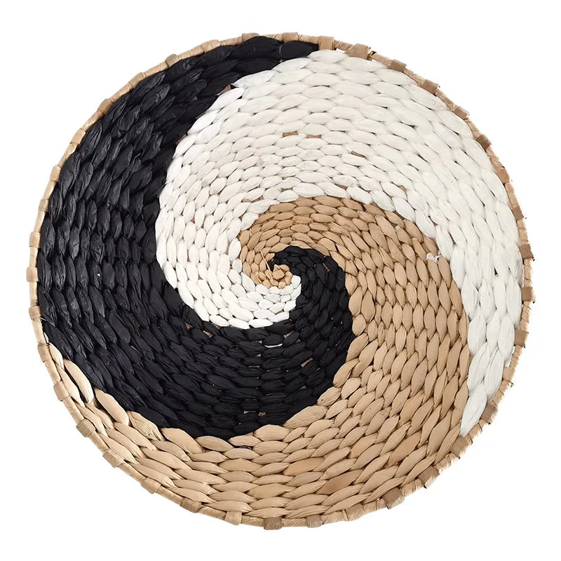 A round woven straw wall decor hanging featuring a black and white spiral design.
