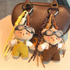 Our teddy bear keychain wearing yellow overalls and aviator glasses attached to a brown leather bag.