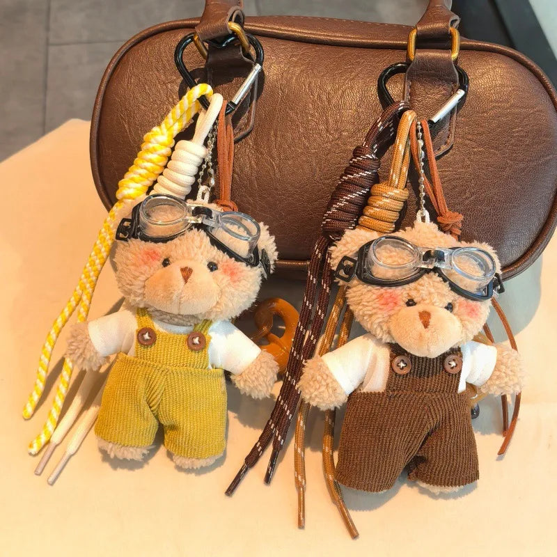Our teddy bear keychain wearing yellow overalls and aviator glasses attached to a brown leather bag.