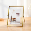 A modern gold-framed picture frame displaying a minimalist landscape with a vase and a small painting.