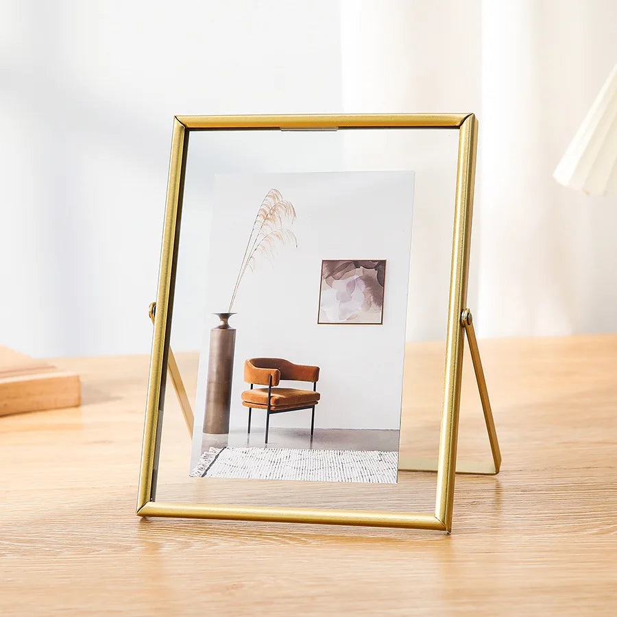 A modern gold-framed picture frame displaying a minimalist landscape with a vase and a small painting.