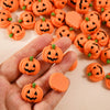 A hand holds a collection of 20 small, orange resin pumpkin charms for fall decor.