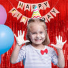 A smiling young girl with white frosting on her hands is in front of a red metallic foil fringe curtain birthday banner.