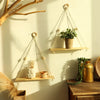 A macrame wood floating wall shelf with hanging rope displaying plants and decorative items on a light-colored wall.