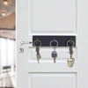 A close-up of a white door with a black hook rack holding three keys and jewelry.