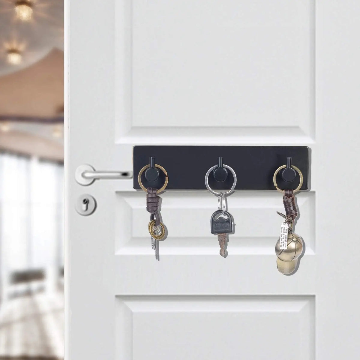 A close-up of a white door with a black hook rack holding three keys and jewelry.