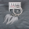 A dream catcher pendant featuring a crystal mirror, beads, and white feathers displayed on a white wooden rack.
